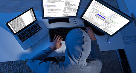 Ein Hacker vor drei PC-Bildschirmen