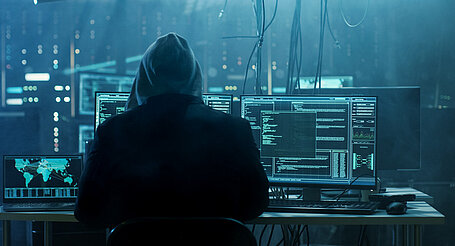 Ein Hacker vor drei Bildschirmen