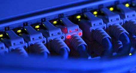 Ein Netzwerk-Kabelstecker leuchtet in der Netzwerkzentrale zur Kontrolle rot